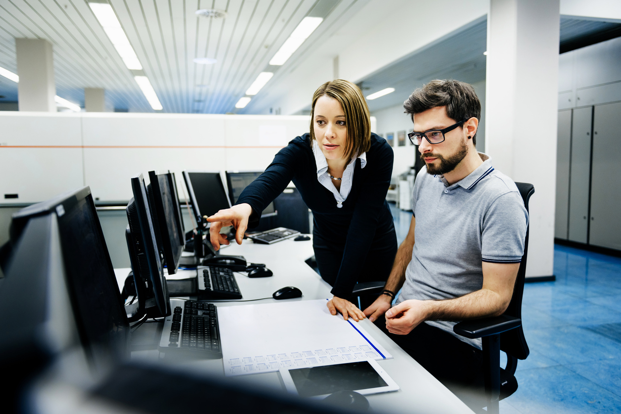 Two IT professionals in a big control room of a factory talking.