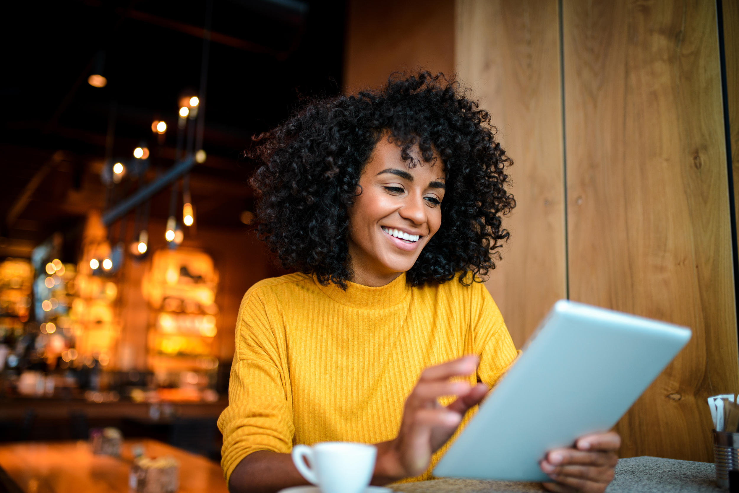 Beautiful smiling African American woman using digital tablet at the bar.