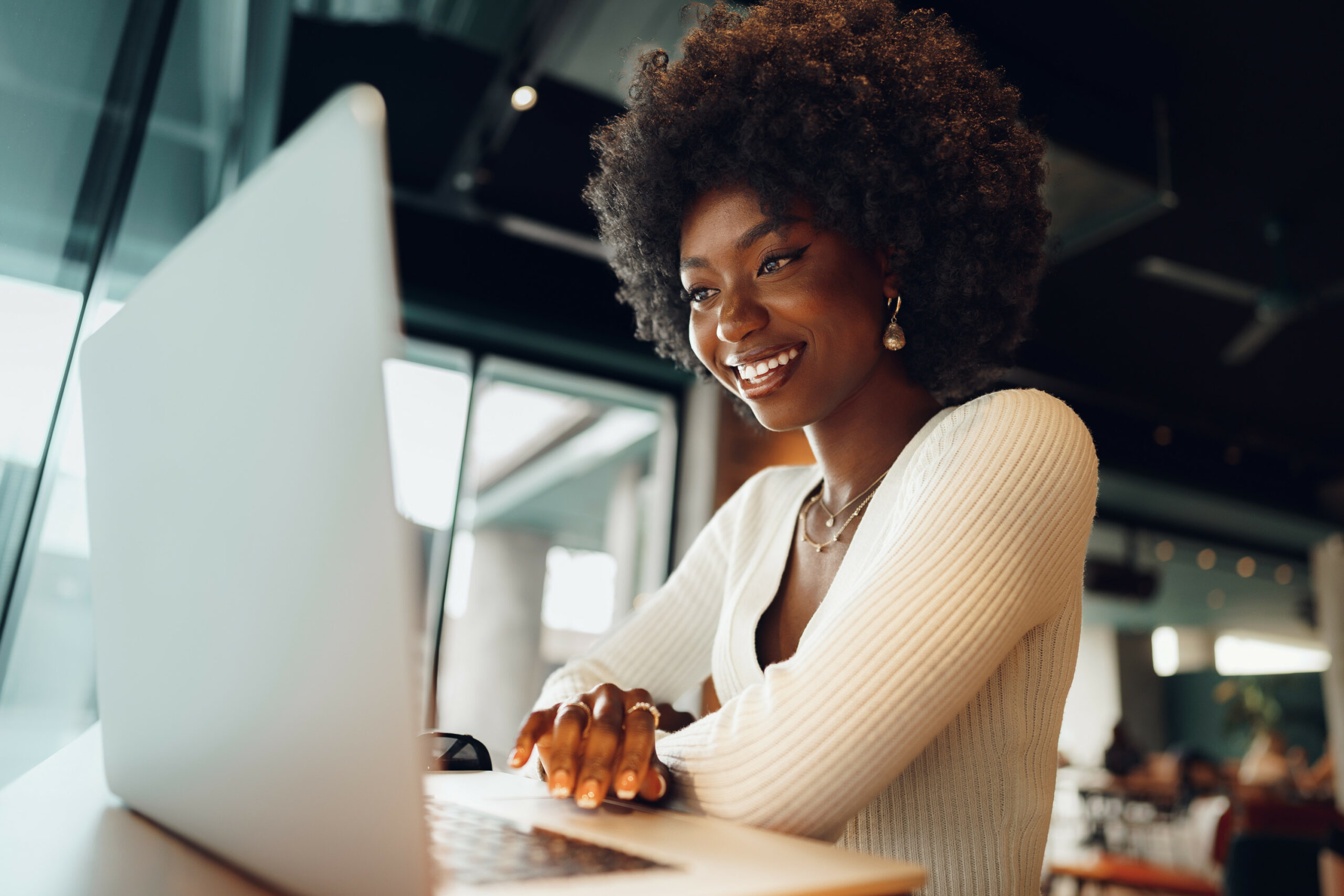 Smiling young african woman sitting with laptop in cafe, portrait